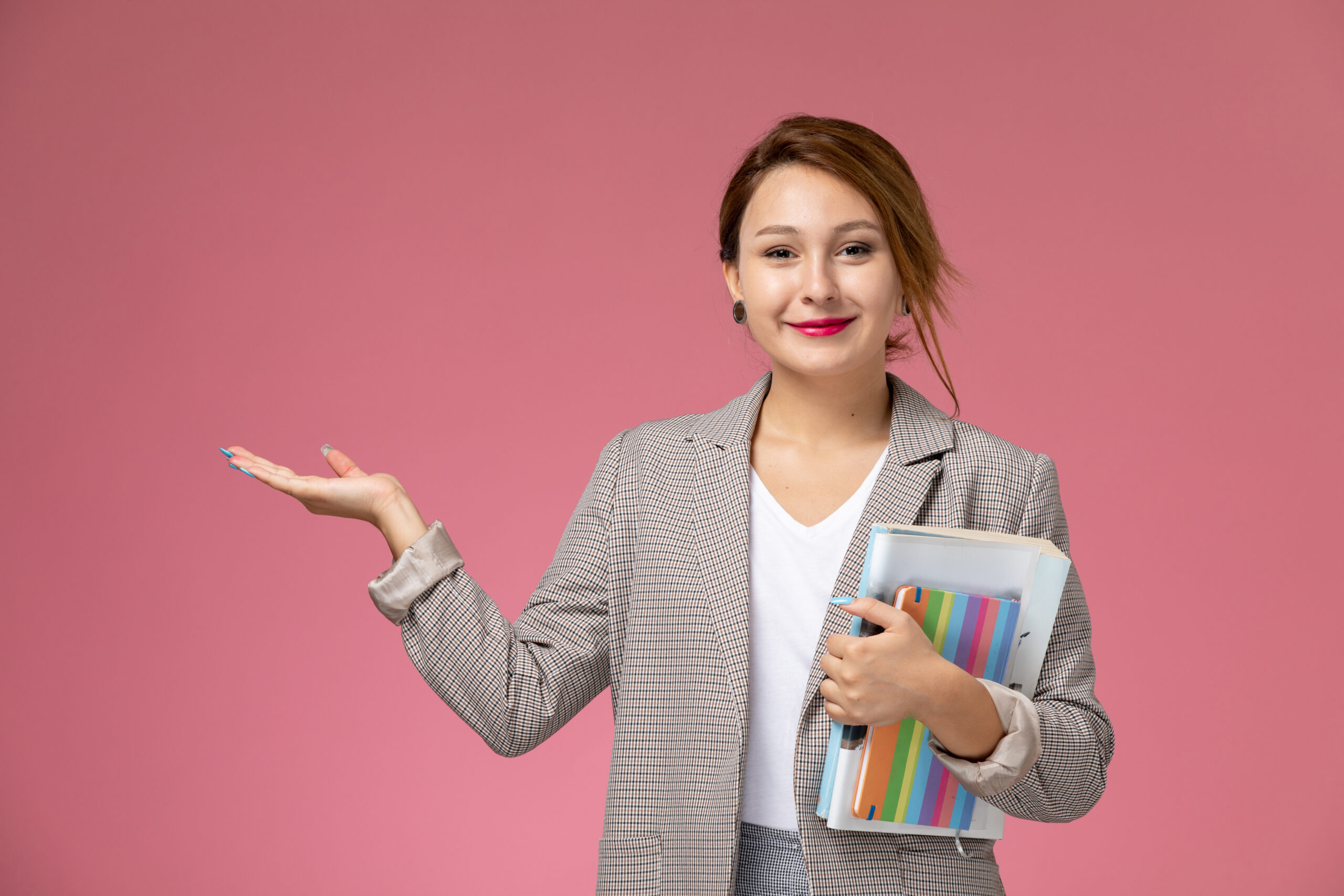 front view young female student white t shirt grey coat grey trousers with copybook her hands smiling pink desk lessons university college study